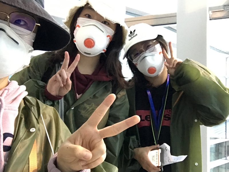 This is a picture taken of three women who are all wearing hats, face masks, and coats flashing a peace sign at the camera. 