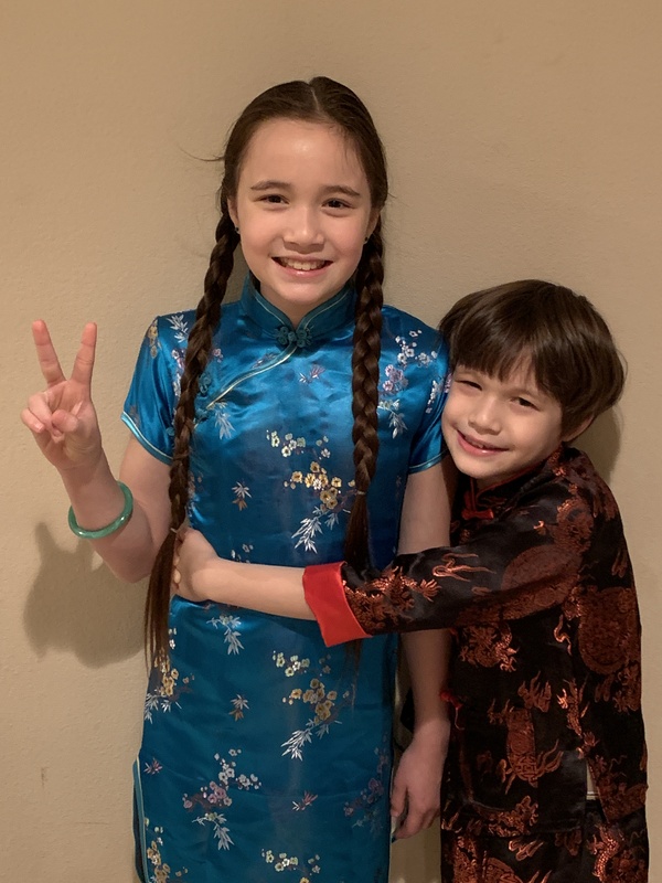Two children in silk kimonos for Chinese New Year displaying the peace sign with their hands.