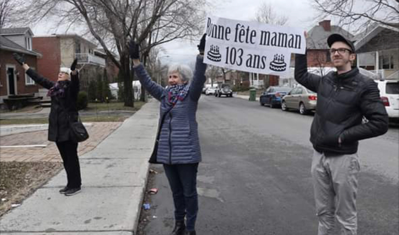 Three people with a sign reading "Bonne fete maman 103 ans".