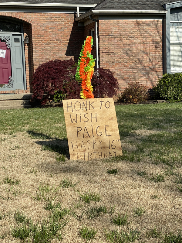 A wooden sign in a front yard reading "Honk to wish Paige Happy 16th Birthday".