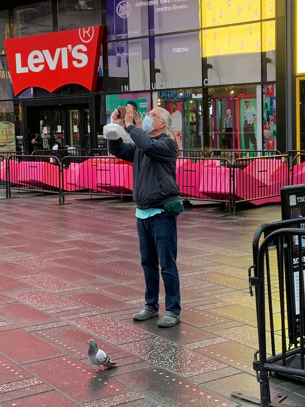 A person with a mask standing next to a pigeon taking a picture.