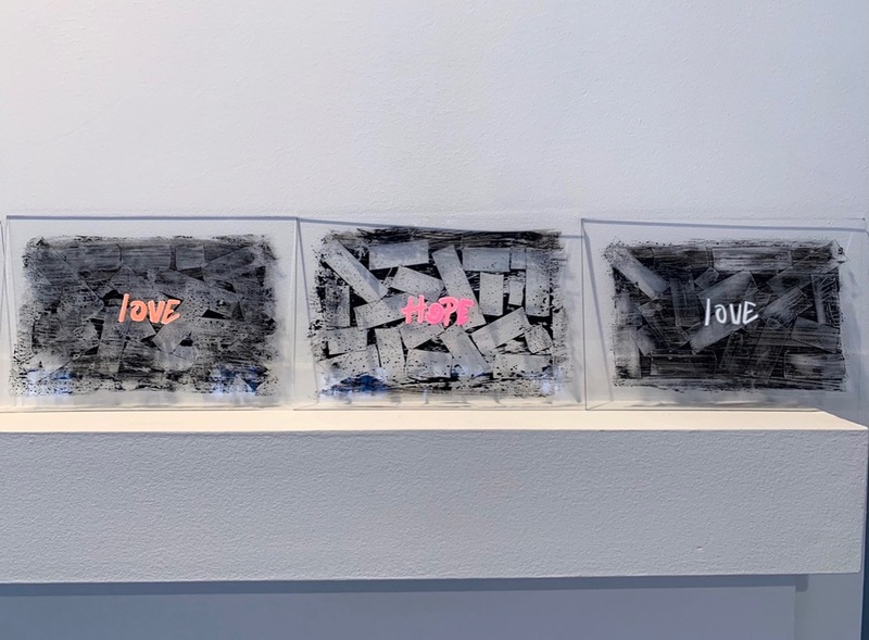 This is a picture taken of three abstract paintings, each made with dark grey colors and messages in the center that read "love" and "hope". 
