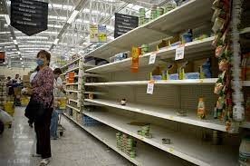 This is a picture taken of several shoppers wearing face masks scouring the mostly empty shelves of a grocery store.