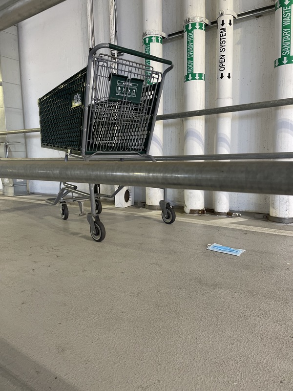 This is a picture of a face mask that has been discarded by a Whole Foods shopping cart in a parking garage. 