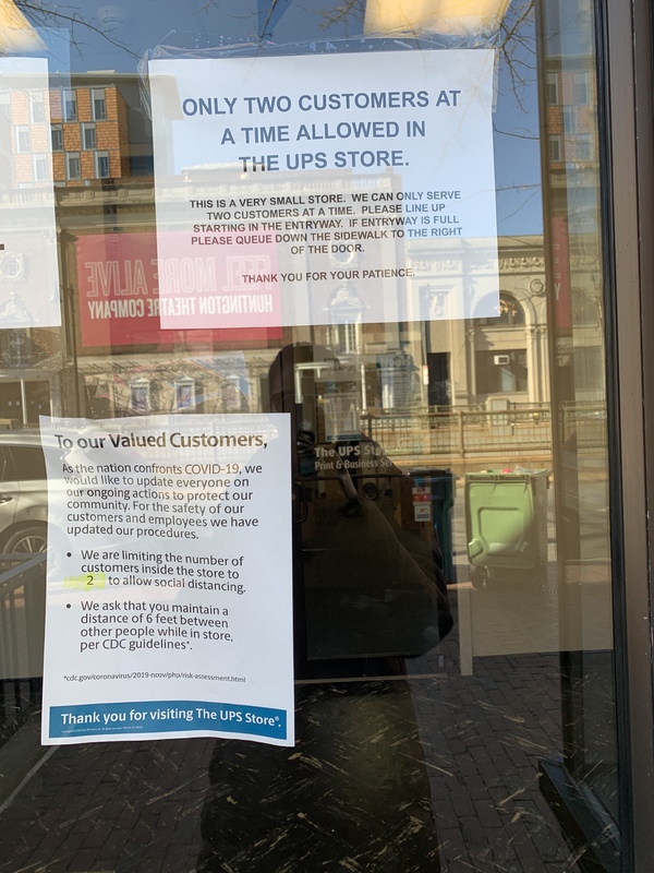 A piece of paper that is taped to the inside of a window informing customers about limiting how many people will be in their store and to practice social distancing. 