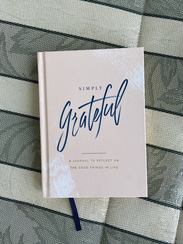 A white book cover reading "Simply Grateful: A Journal To Reflect On The Good Things In Life". 