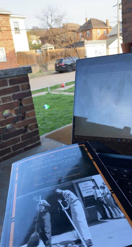 This is a picture taken of a book resting on a laptop which is sitting on a persons lap on a front porch. The book title reads "From Store Front to Monument".