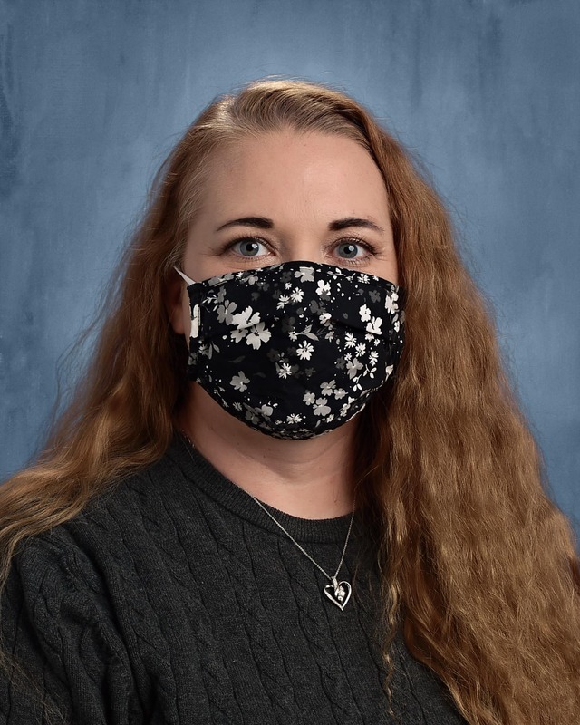 This is a picture of a woman wearing a flower print black face mask, and a silver heart pendant. 