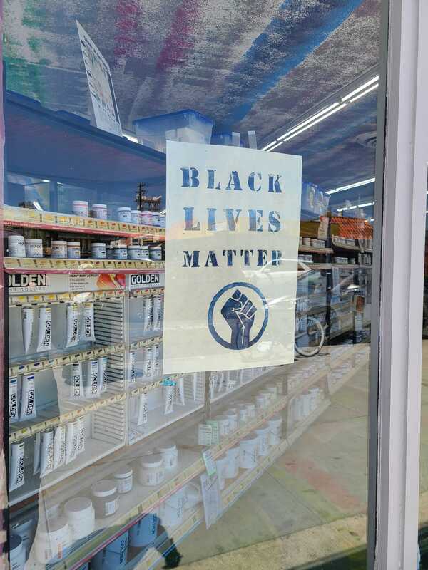 This is a picture of a sign in a storefront window which reads "Black Lives Matter", followed by the Black Power Movement symbol of a raised fist. 