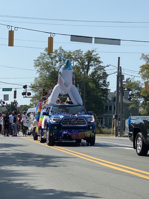 This is a picture of an inflated unicorn attached to the back of a truck, which is taking part in a Pride Parade celebrating LGBTQ culture. 