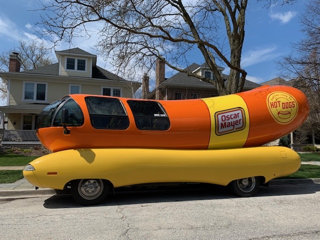 A hotdog shaped car parked in front of a house. 