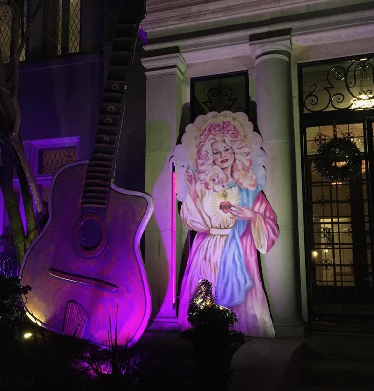 This is a picture of a decorated house. A giant acoustic guitar flanks the entrance to the home along side the cardboard cutout of a woman in a robe. 