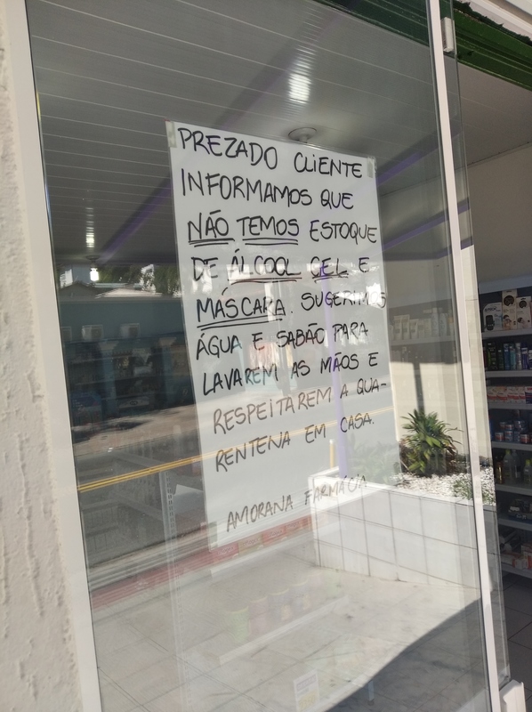 A white sign is taped on the inside of a glass window. The sign is in Portuguese translated into English the sign says: "Dear customer, we inform you that we do not have stock of alcohol, gel and mask, We suggest soap and water to wash your hands and respect quarantine at home".