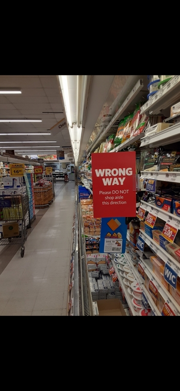 Photo down a grocery aisle with a red sign with text, "WRONG WAY - PLEASE DO NOT SHOP AISLE THIS DIRECTION"