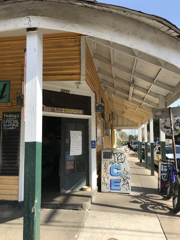 A yellow and white corner store that has its black front door propped open. The right door has a paper sign taped on the front. 
