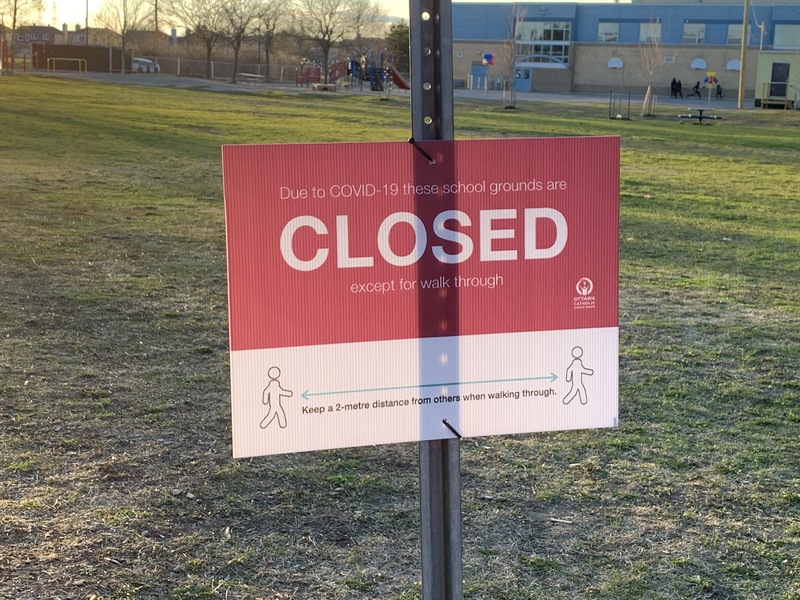Image of a sign in front of a school which reads due to Covid-19, these school grounds are closed except for walk-through.