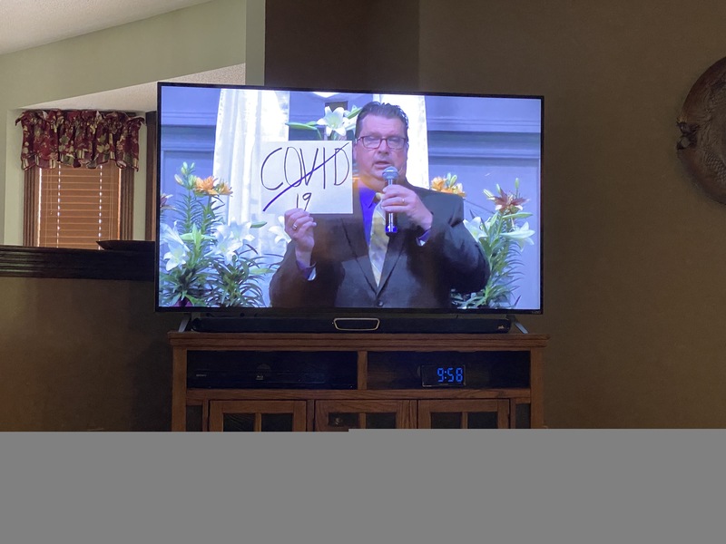 A TV screen featuring a man holding a sign with COVID-19 crossed out on it.