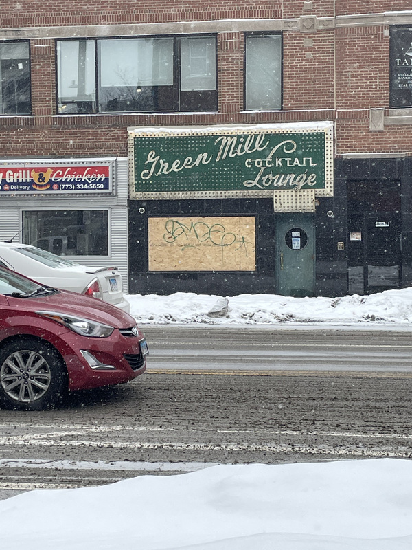 This is a picture taken of a sign for a cocktail lounge from the street on a snowy day. The sign reads "Green Mill Cocktail Lounge".