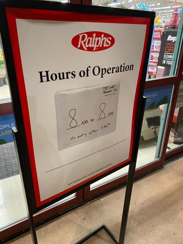 A sign to a grocery store that displays hours of operation. 