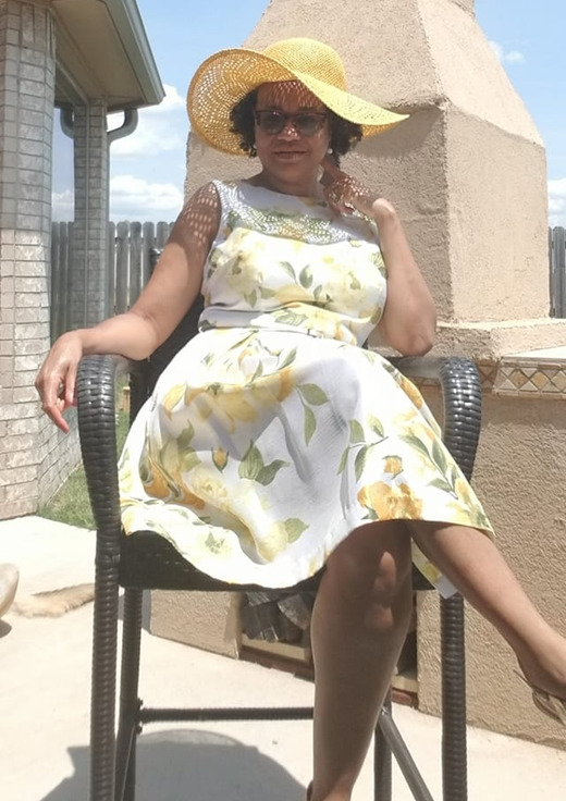 This is a picture taken of a woman wearing a sun dress, sitting in a chair. 