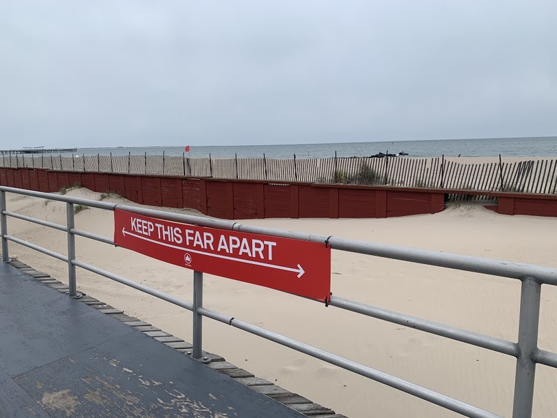 a red sign tied to a railing showing how far apart people need to stay