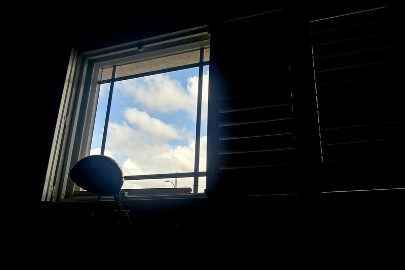 This is a picture taken from the inside of a dark room of the view of the sky through a window. 