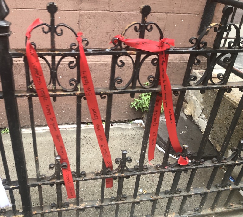 This is a picture taken of red ribbons wrapped around sections of a black iron fence. 