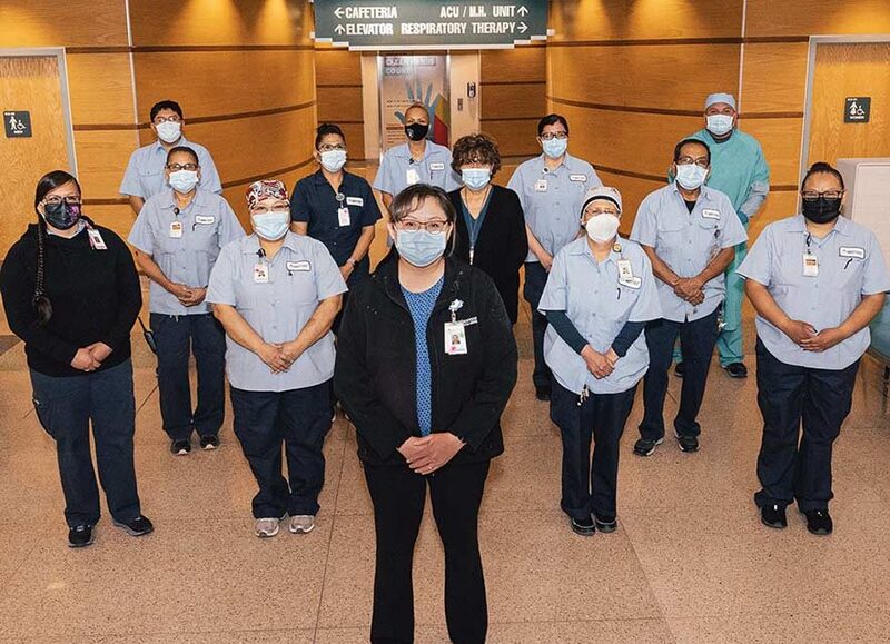This is a picture of a group of healthcare workers standing in the lobby of a building. Everyone is wearing a face mask. 