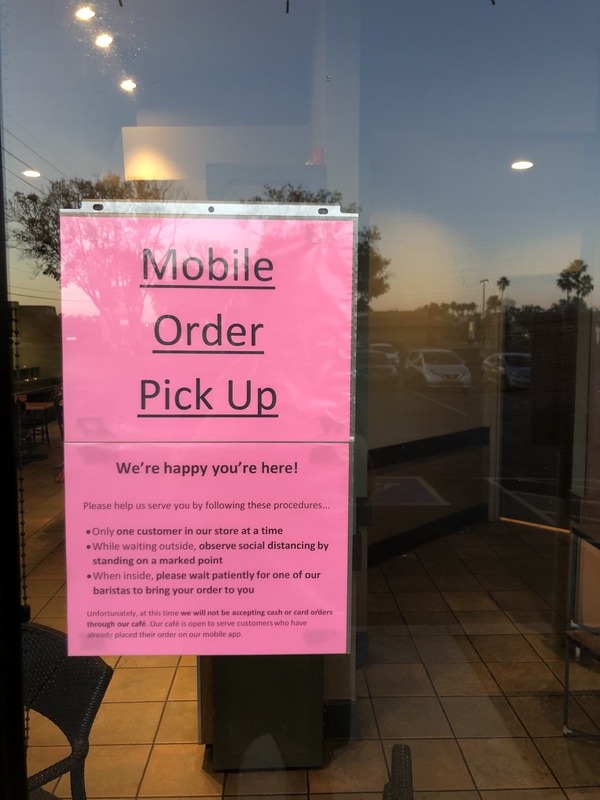 A pink sign on a glass door explaining the rules for mobile pick up at a restaurant during lock down restrictions 