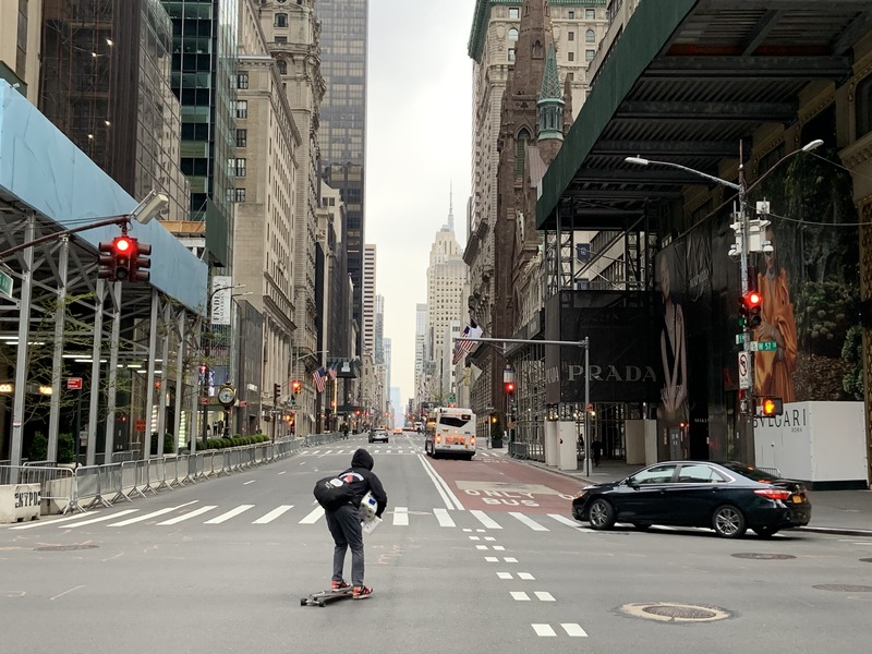 A person skateboarding down an empty street with tall buildings. 