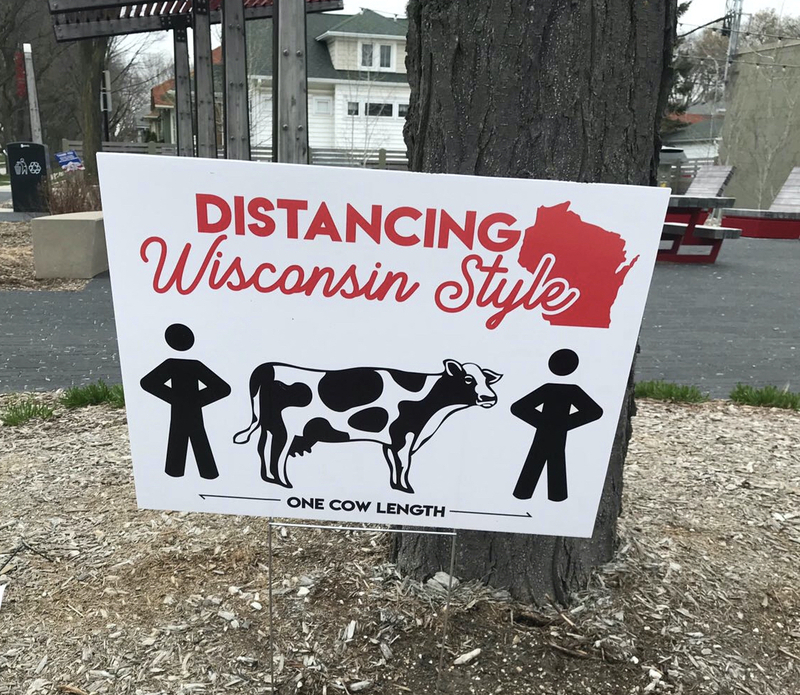 A sign that states "Social Distancing... Wisconsin Style: One Cow Length". 