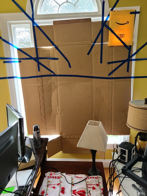 A cardboard box is taped over a window with blue tape. 