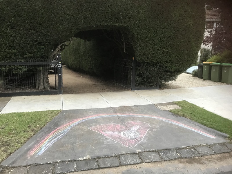 A sidewalk chalk rainbow with a heart drawn underneath it at the end of a residential driveway.