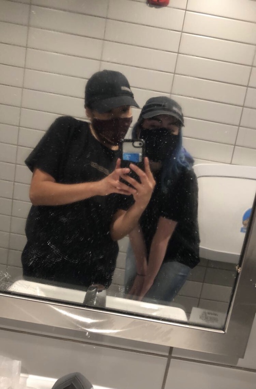 This is a mirror picture of two people wearing a work uniform and face masks. 