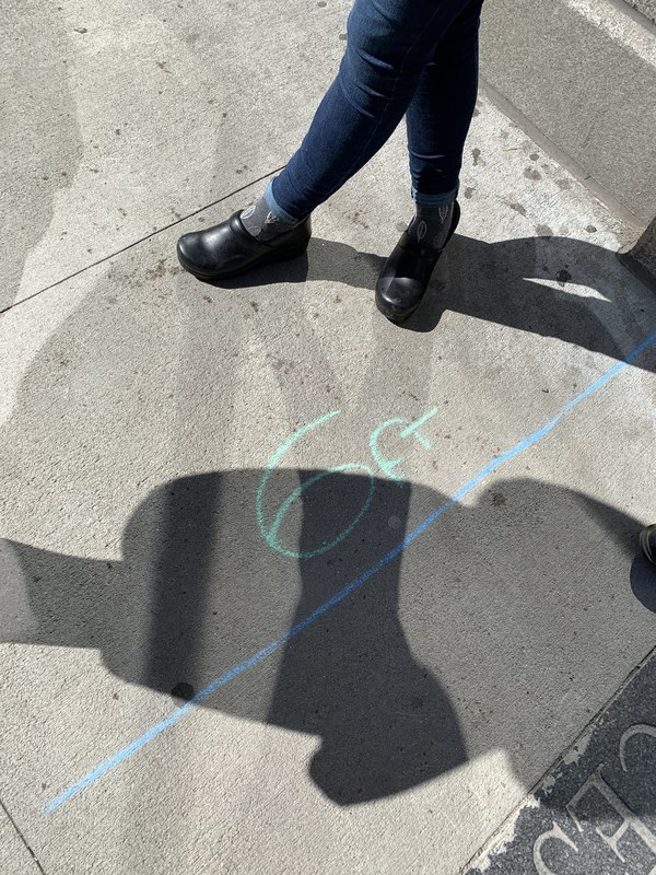 A sidewalk has measurements drawn on it with chalk to indicate 6 feet of distance for social distancing. 