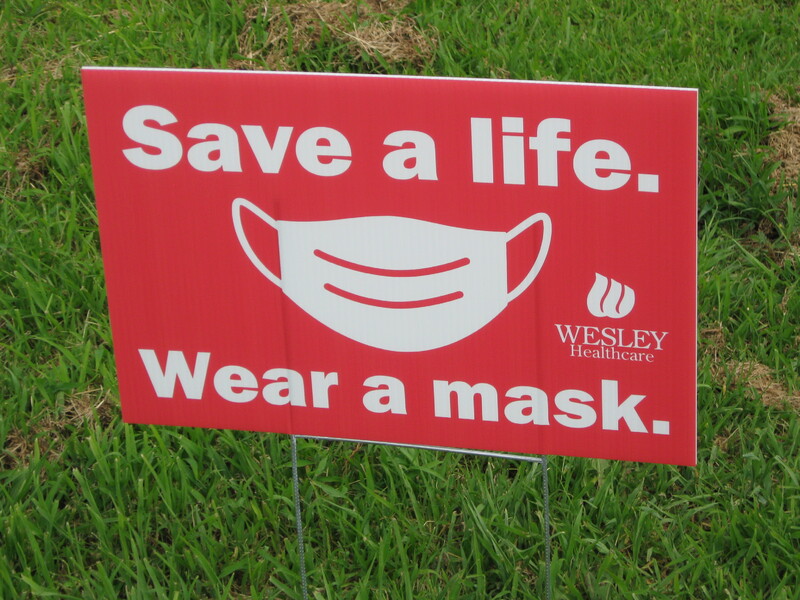 A red yard sign reading "Save a life. Wear a mask" with a graphic of a mask. 