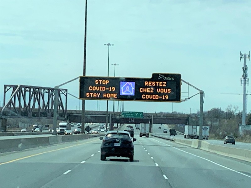 Image of a sign on the highway in both English and French which says stop Covid-19, stay home.