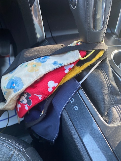 This is a picture of a collection of different designs of reusable face masks hanging off of the gear shift in a car. 