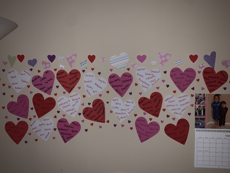 Colorful paper hearts with names written on them taped to a wall.