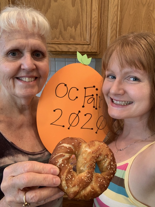 Two adults holding a pretzel and a sign that reads "OC Fair 2020".