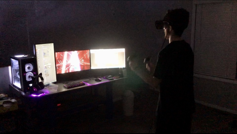 A person in front of three computer monitors playing on the Oculus headset.