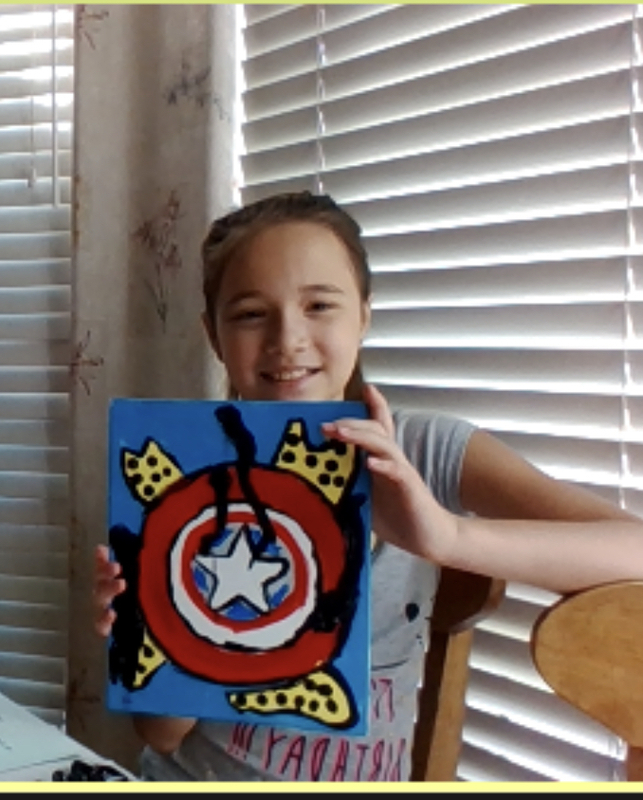 Young girl holds up painted canvas of Captain America shield.