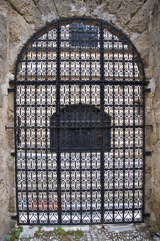 This is a picture taken of an ornate iron gate that has been installed in a stone archway. 