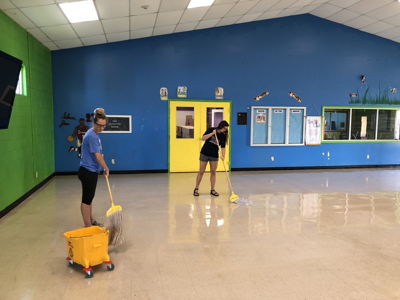 This is a picture taken of two women mopping a floor. 