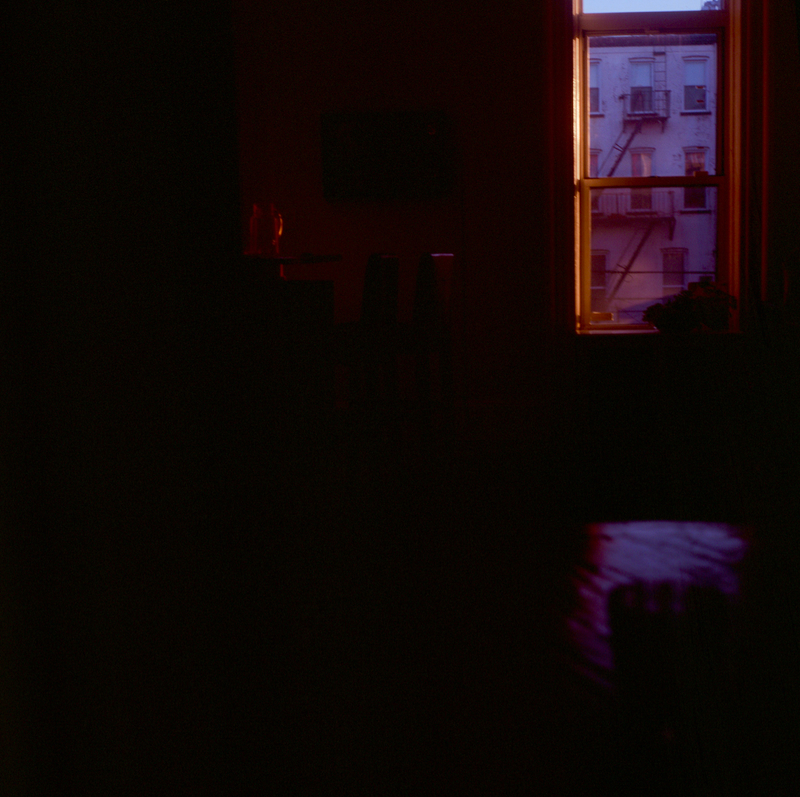 A picture of a dark bedroom from the inside, with a window in the foreground showing the first light of dawn. 