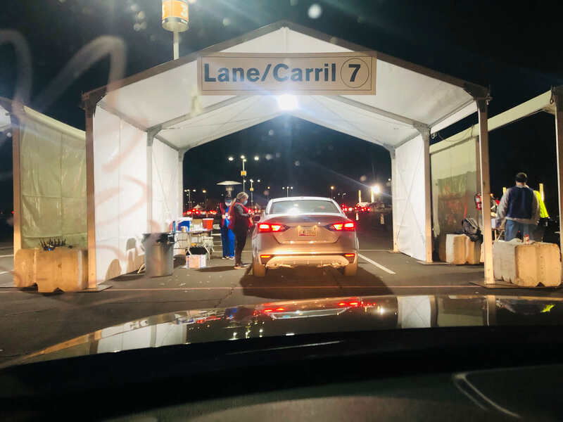 Vehicle at night below sign that reads "Lane 7/Carril 7" during drive-thru COVID-19 vaccination.