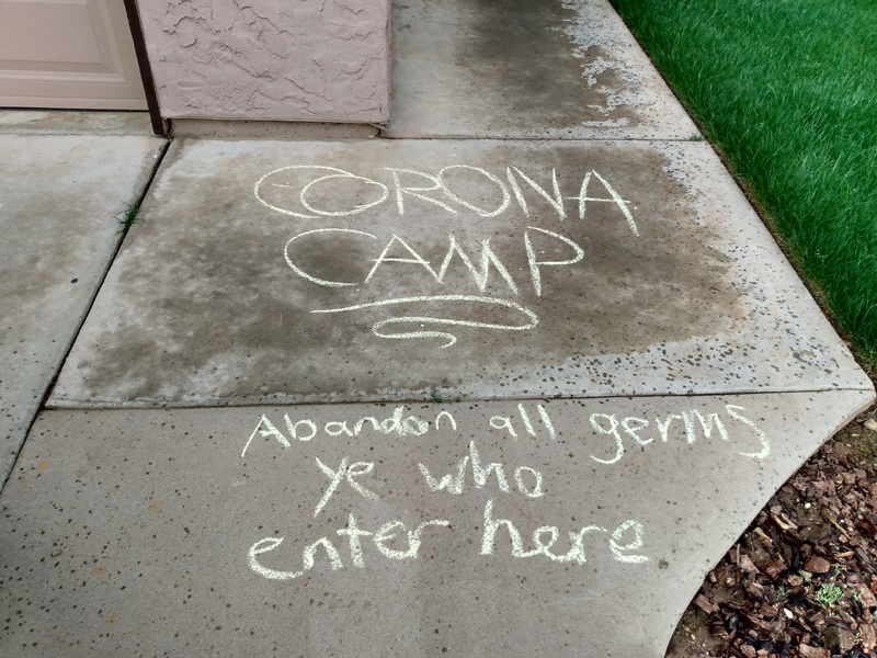 The words "Corona camp, abandon all germs ye who enter here" written with chalk on a sidewalk. 