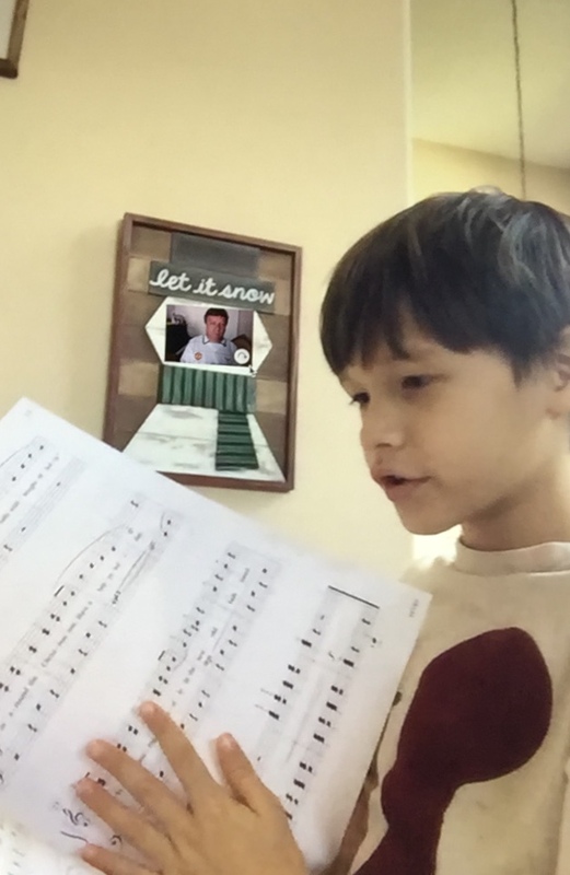 Boy holding sheet music with photo of piano teacher in Christmas frame behind him.