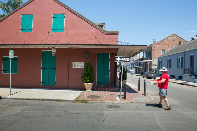 A person crossing a vacant street by a red building.