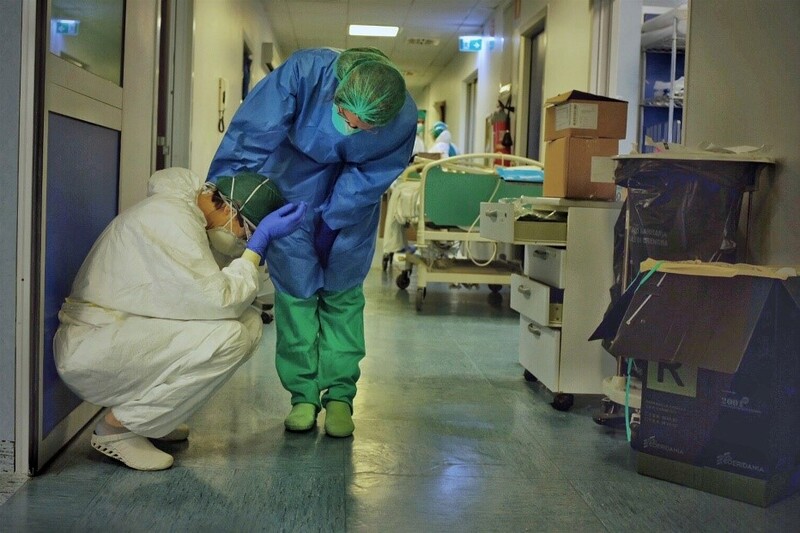 A distressed healthcare worker on the floor in a hospital being comforted by another healthcare worker.